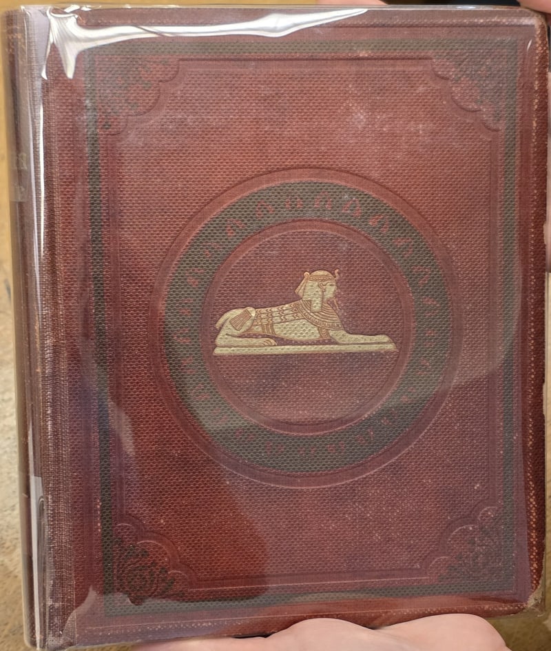 Original red cloth front cover with gilt sphinx and green-stamped band, borders, and corner ornaments, in a protective jacket
